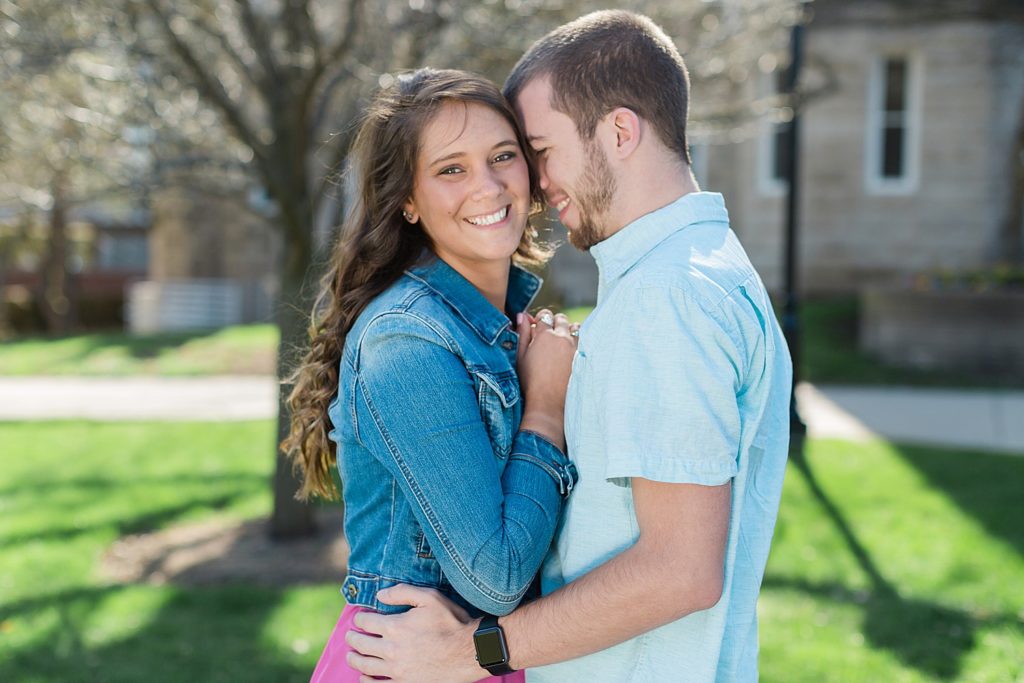 Girl smiling at camera while fiance cuddles head into her face with the sun behind them. 