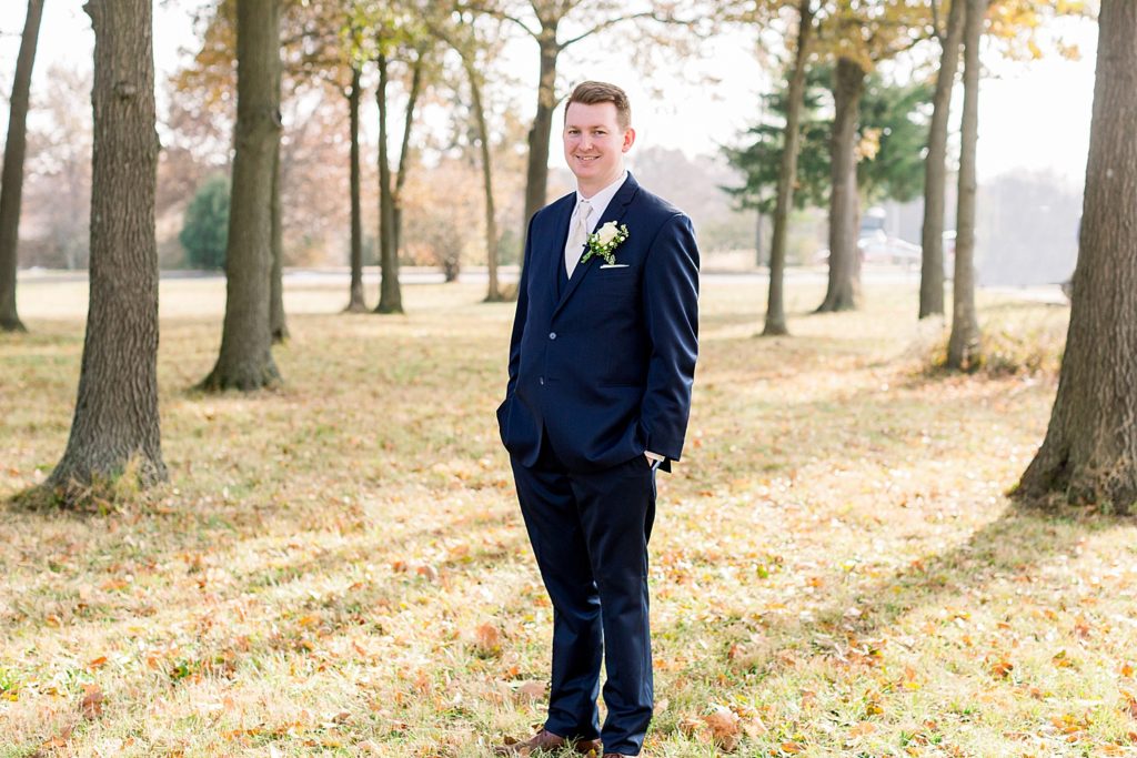Posed photo of a groom on his wedding day standing in the woods with the sun behind him. 