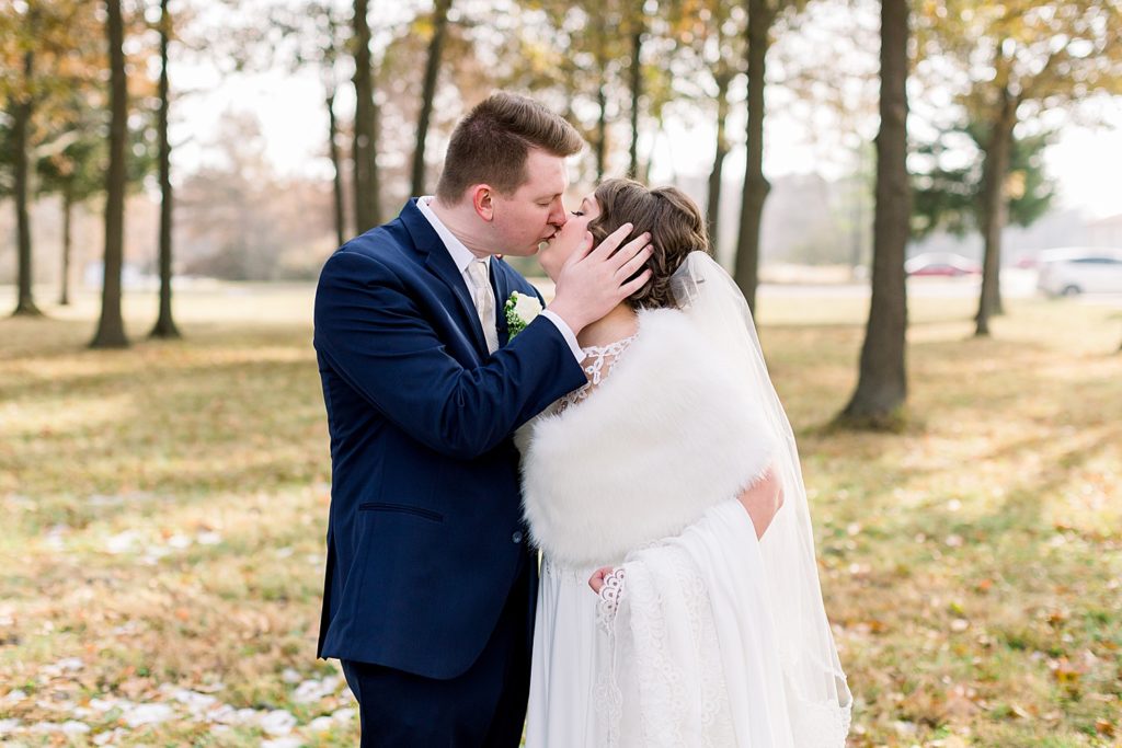 Bride and groom kissing on their wedding day. The bride is holding the skirt of her wedding dress with a warm white fur around her shoulders. 