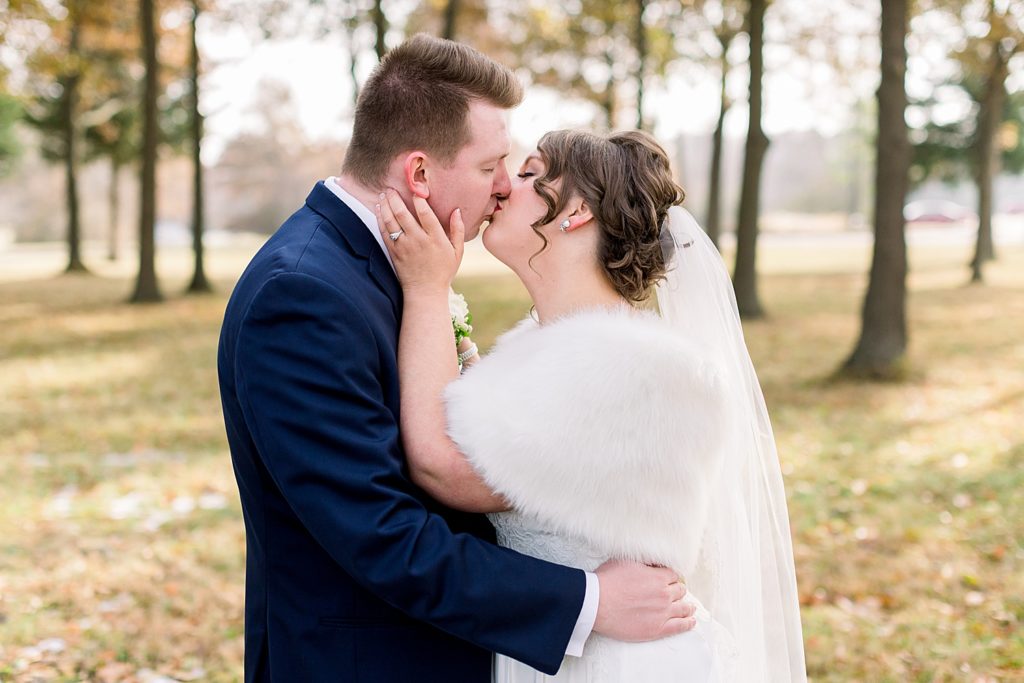 Bride and groom kissing. The bride is wearing a white fur around her shoulders. 