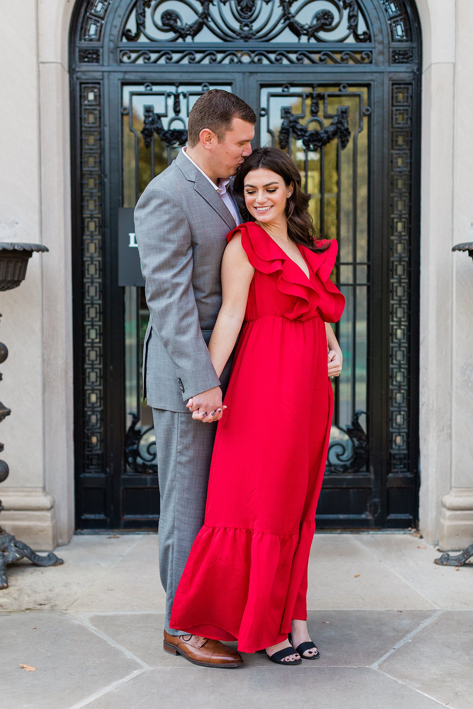 Couple posing for engagement photos at the Lilly House. The girl is wearing a long red dress and the man is wearing a light grey suite. 