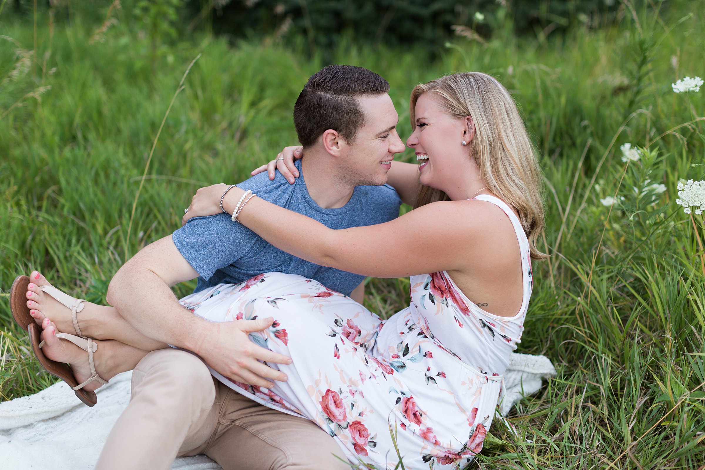 Couple sitting on blanket in the grass looking at each other for engagement photos with Jennifer Council Photography.